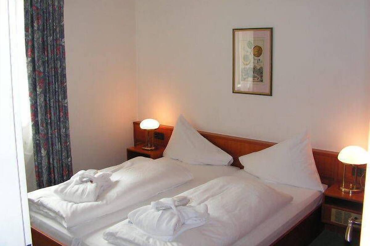 A hotel room with two beds, white linens, a framed picture on the wall, and bedside lamps.