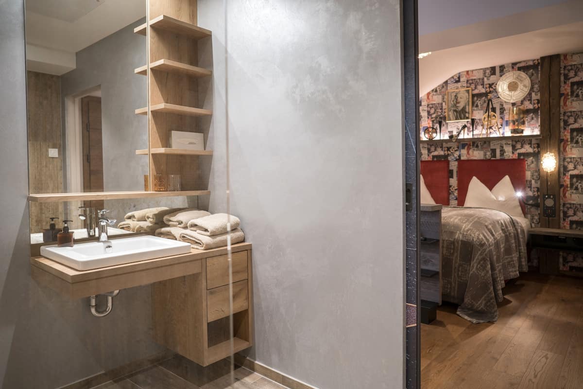 Ein modernes Badezimmer mit einem großen Spiegel, Holzregalen, einem Waschbecken und einem Nachttisch mit einer Lampe.