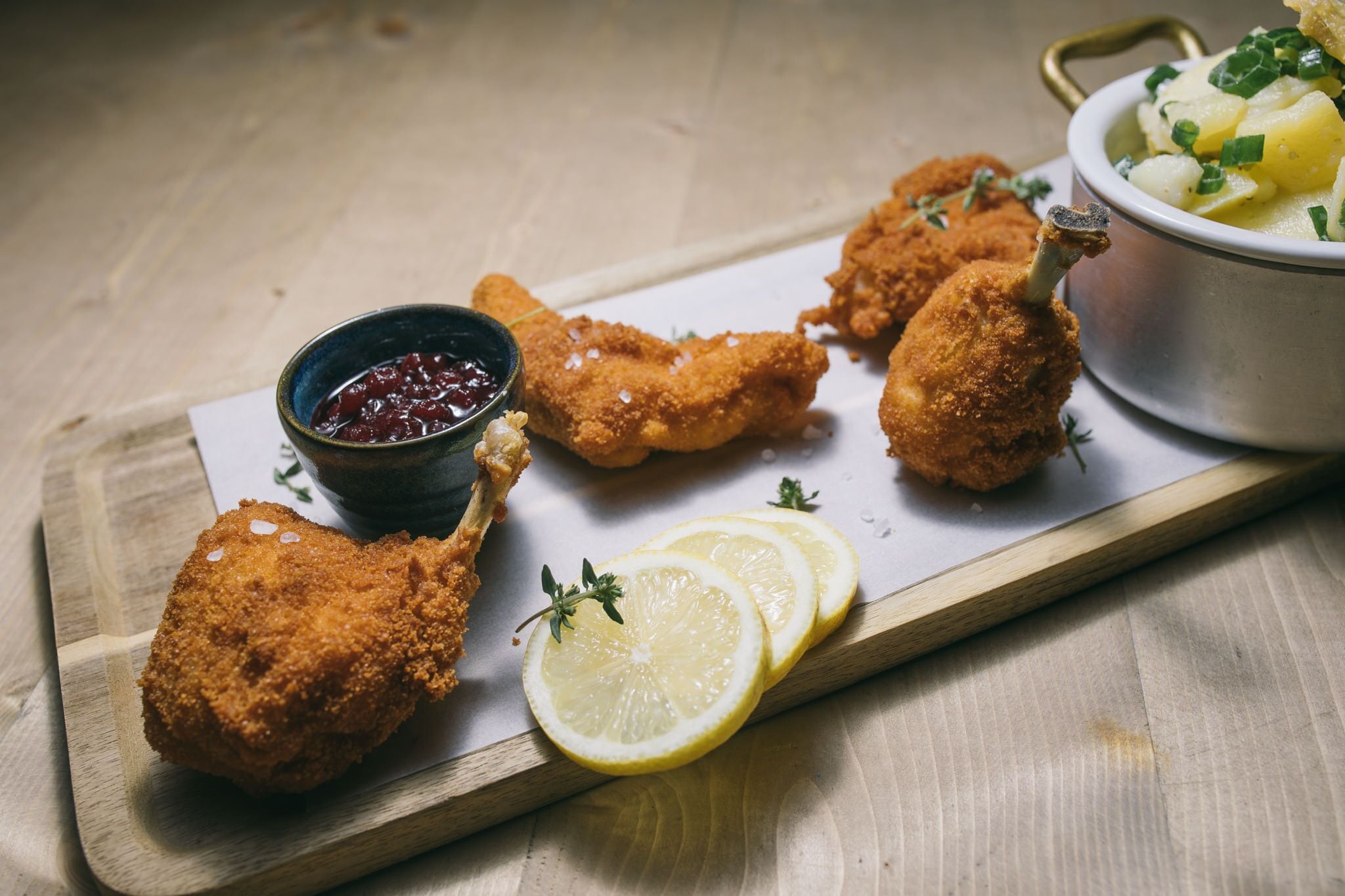 Une planche de service en bois sur laquelle on trouve des morceaux de poulet panés, des tranches de citron et un bol de sauce.