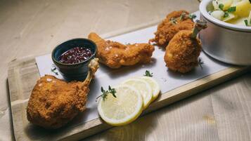 Une planche de service en bois sur laquelle on trouve des morceaux de poulet panés, des tranches de citron et un bol de sauce.
