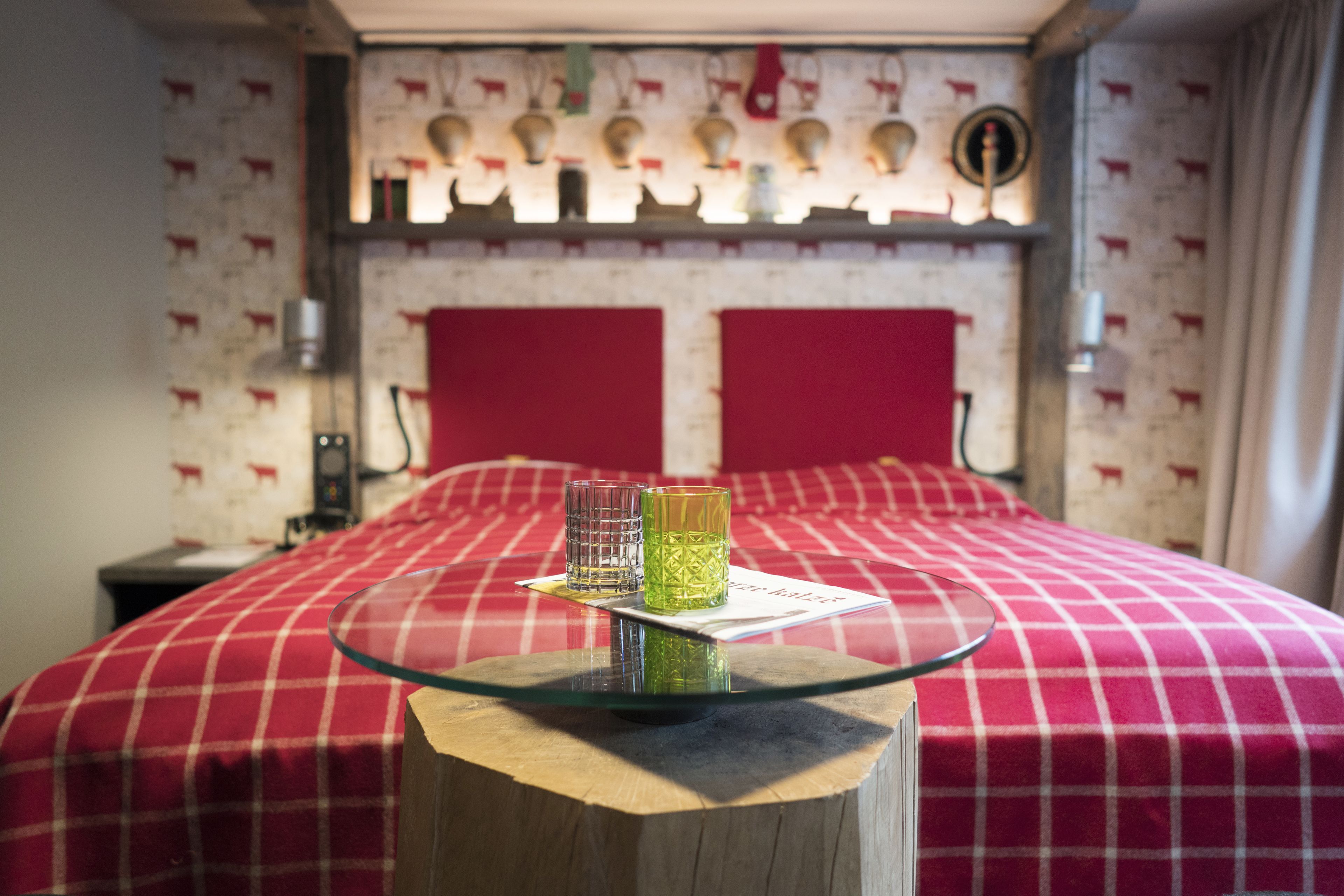 Una cama con una colcha a cuadros rojos, dos cabeceros rojos y una mesa de vidrio con dos vasos y una tarjeta.
