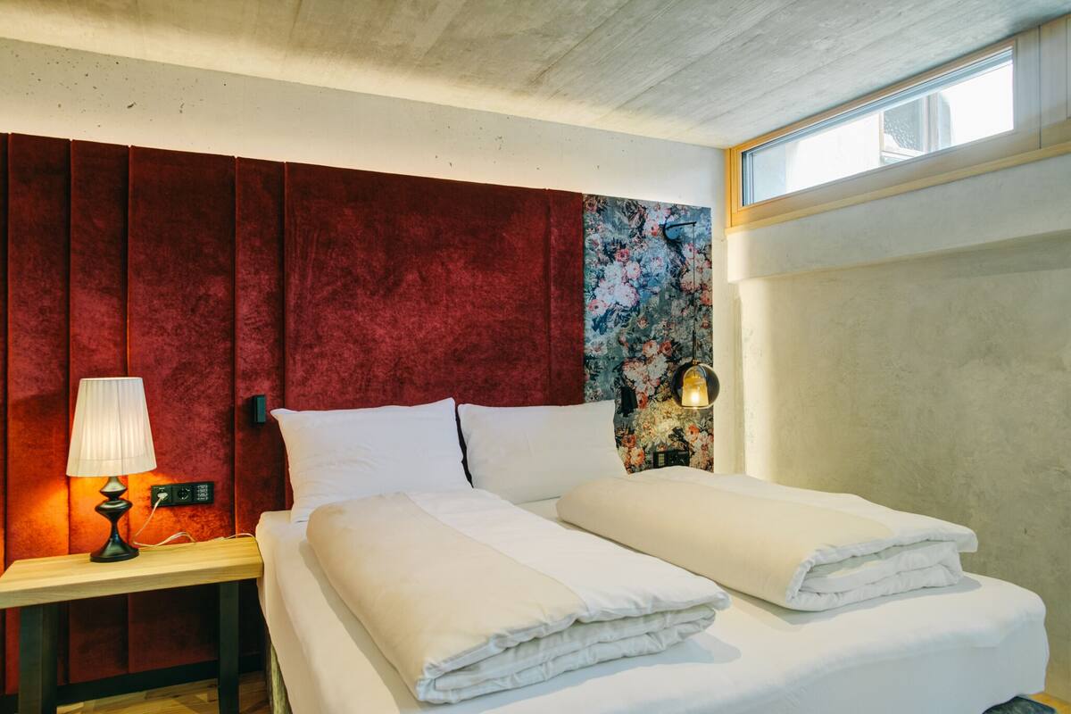 Ein Hotelzimmer mit Bett, Nachttisch mit Lampe, einer Wand mit Blumenmuster und einem Fenster.
