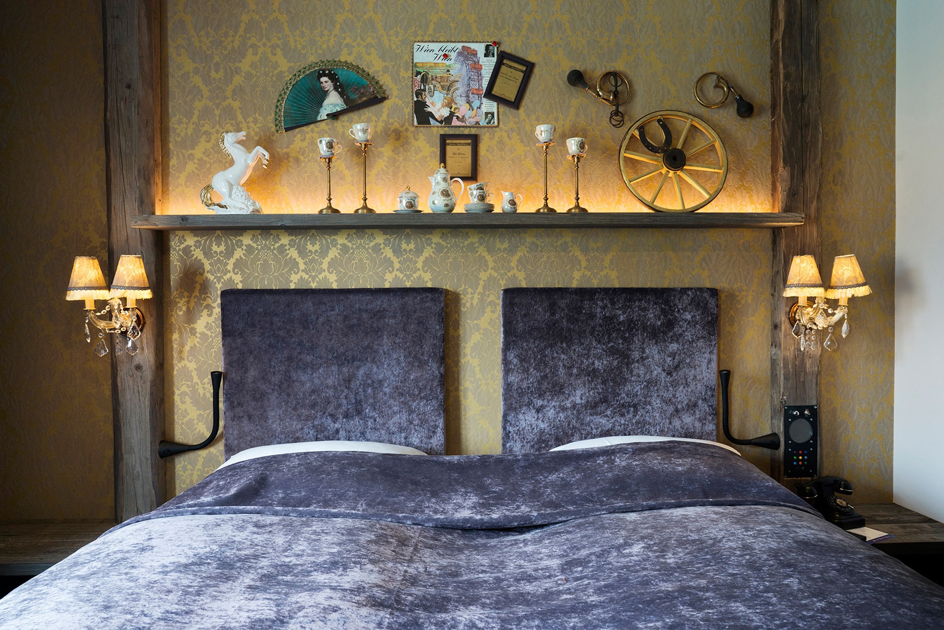 A bed with a dark headboard, two bedside lamps, and a shelf above with decorative items.