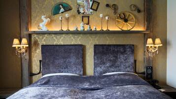 A bed with a dark headboard, two bedside lamps, and a shelf above with decorative items.
