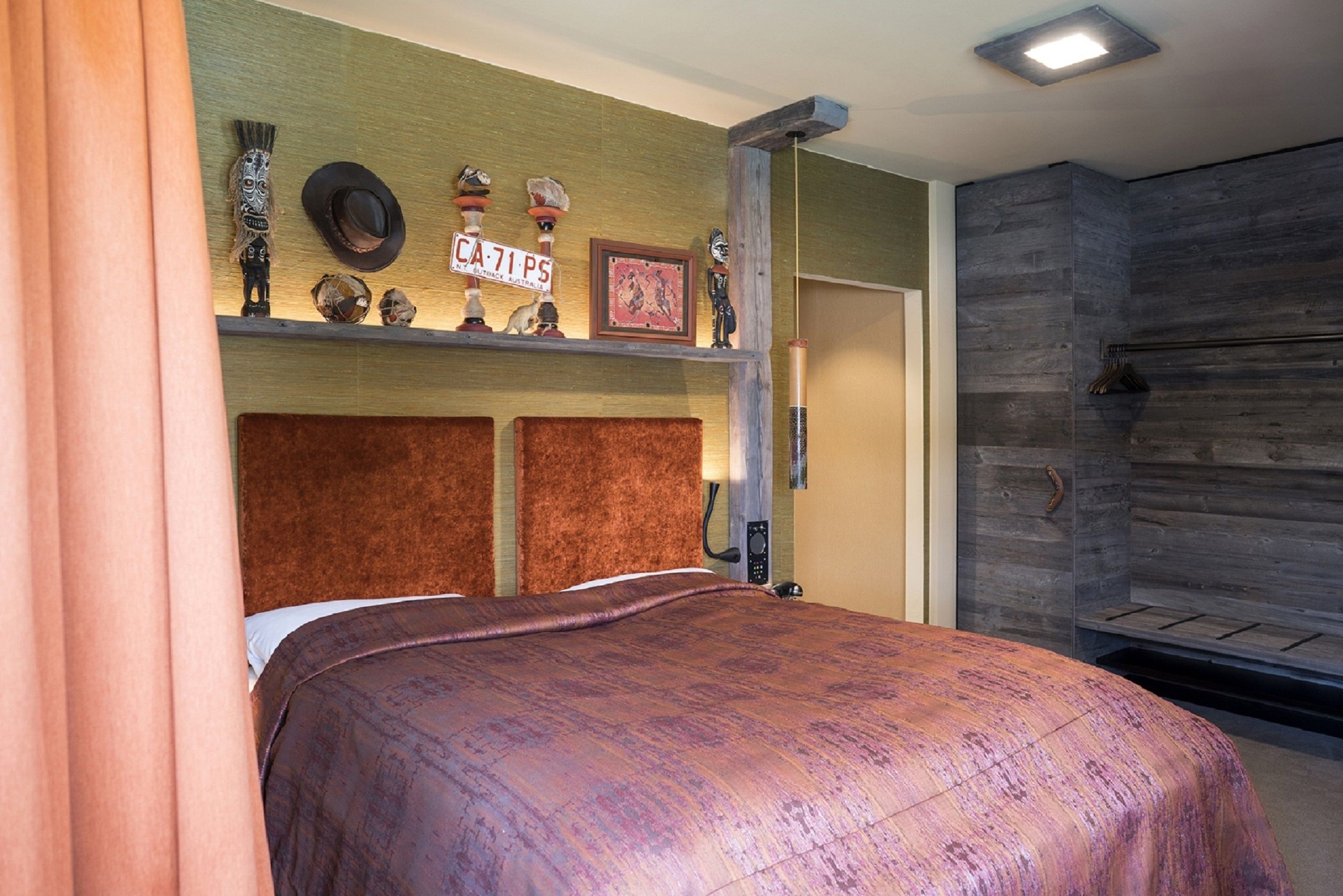 A bedroom with a bed, a shelf with decorative items, a wooden headboard, and a wall with a textured pattern.