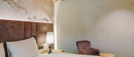 A hotel room with a bed, a nightstand, a lamp, and a chair.