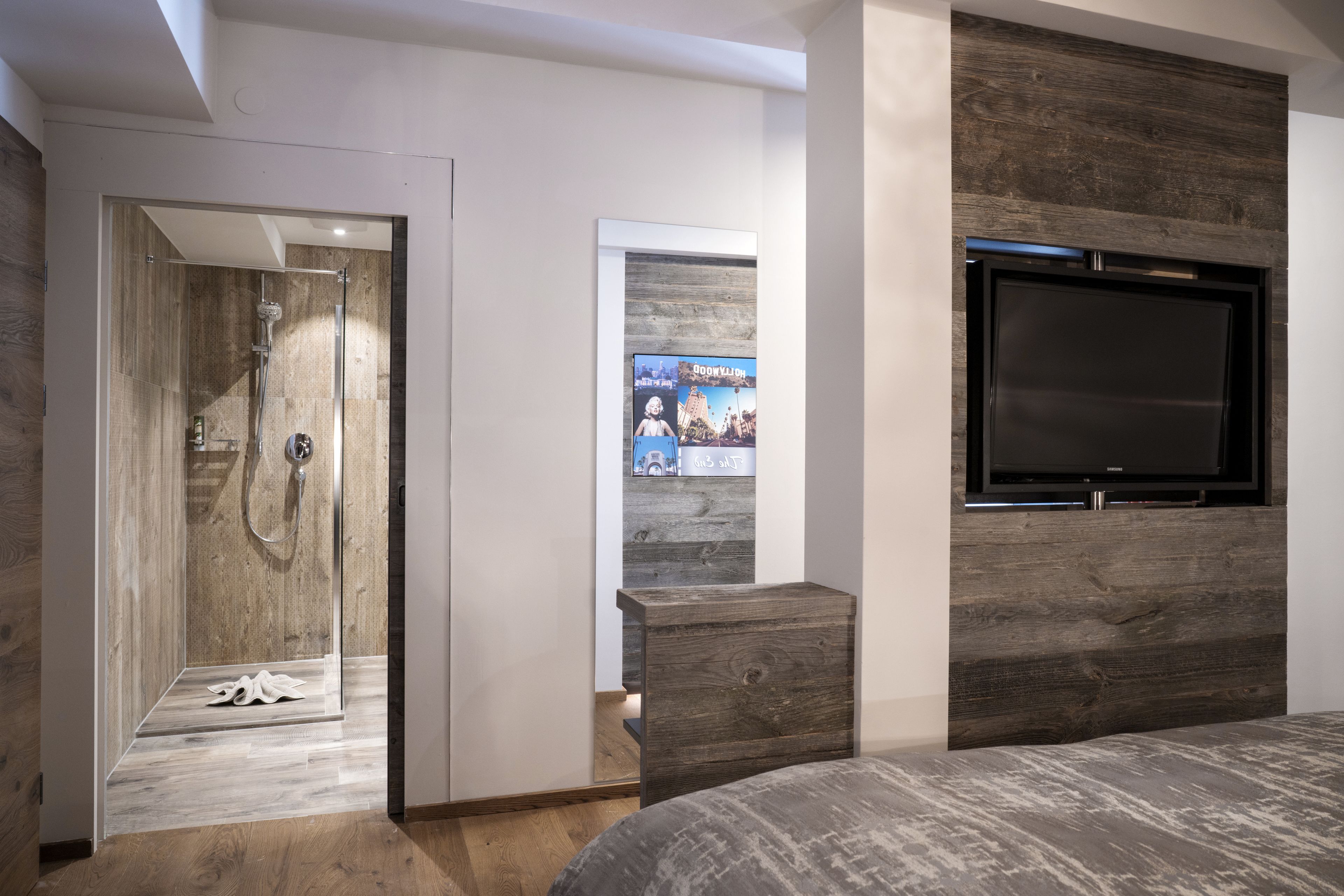 Un dormitorio moderno con cabecera de madera, televisión integrada y zona de ducha.