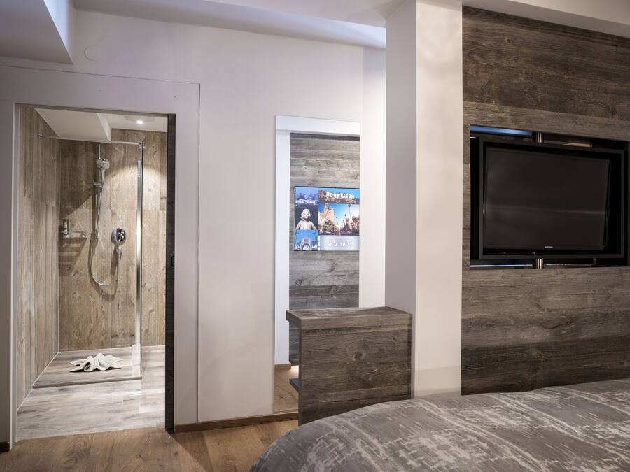 Un dormitorio moderno con cabecera de madera, televisión integrada y zona de ducha.