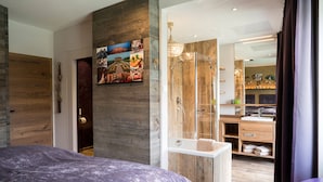 A modern bedroom with a large bed, a wooden wall, a shower area, and a bathroom with a sink and mirror. - Boutique Hotel im Auracher Löchl (Kufstein)