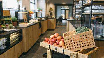 A kitchen area with wooden cabinets, a fruit display with apples and broccoli, and a coffee station with cups and a coffee machine.