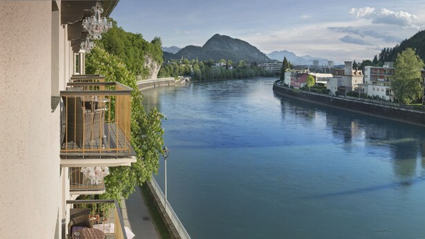 A riverside balcony with wicker furniture, a view of a river, and buildings in the background. - Boutique Hotel im Auracher Löchl (Kufstein)