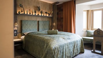 A large bed with a patterned bedspread, a bedside table with a lamp, and a decorative shelf above the bed.
