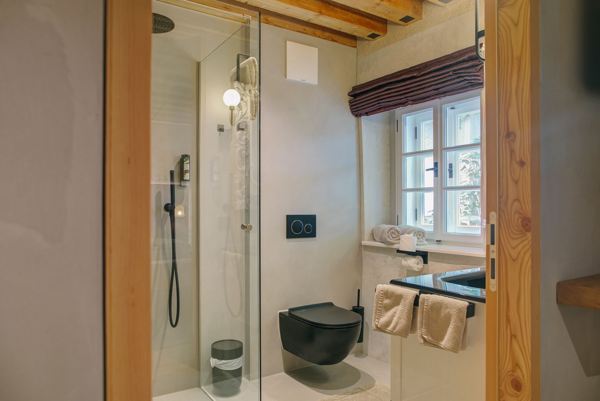 A modern bathroom with a glass-enclosed shower, a black toilet, and a window with curtains.