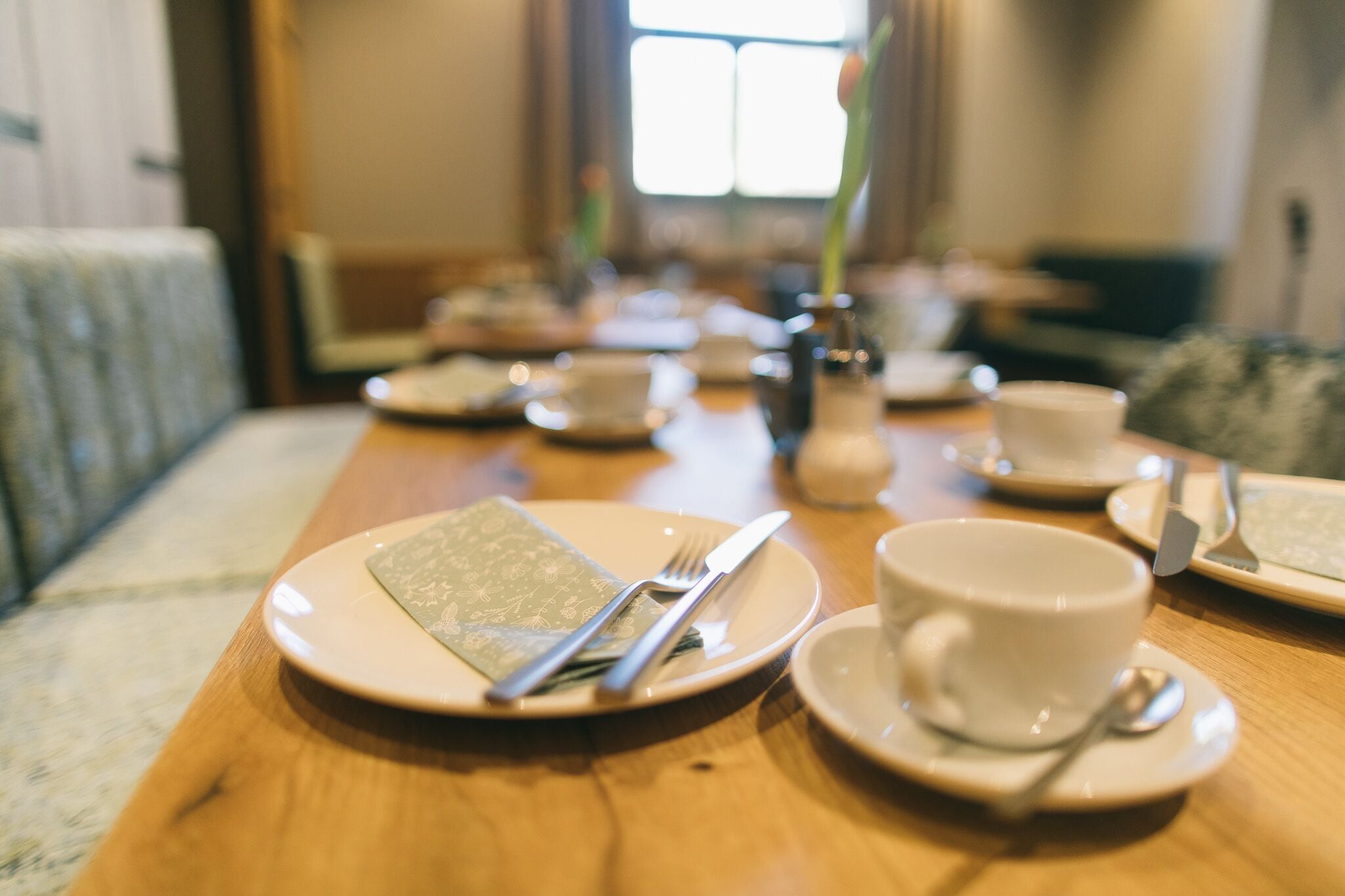 A dining table set with plates, cutlery, and a cup, with a blurred background suggesting a cozy indoor setting.