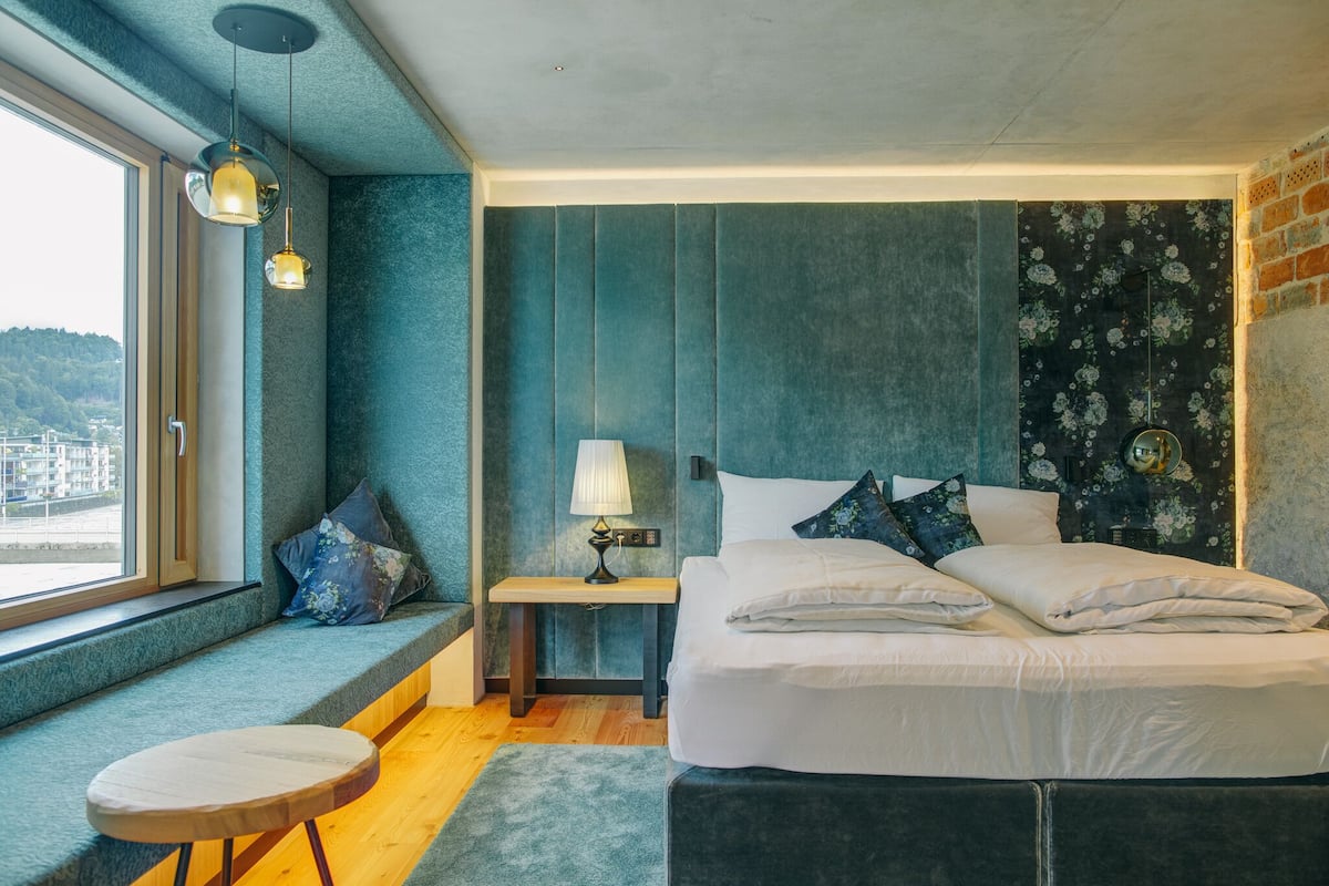 Ein Schlafzimmer mit einem großen Bett, einer Sitzbank am Fenster und Blick auf die Stadt.