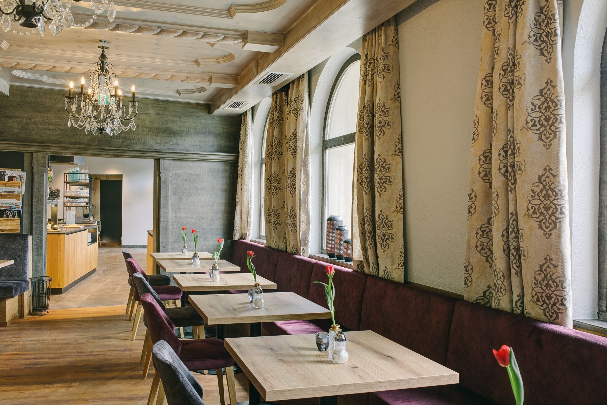 A restaurant with wooden tables, cushioned booths, and a chandelier.