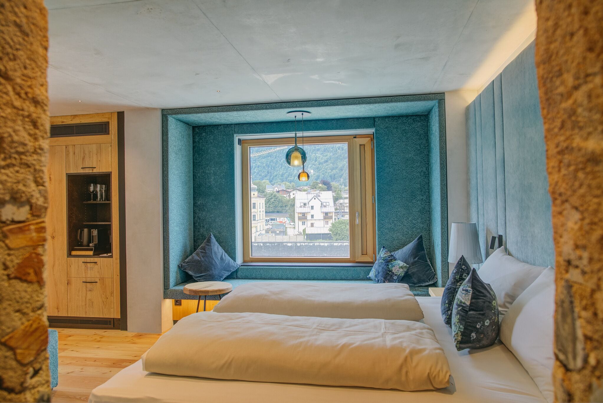 A bedroom with a large window, a bed, a wooden wardrobe, and a small round table.