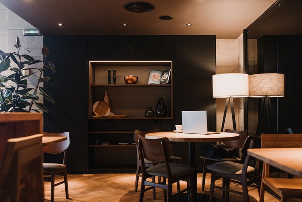 A cozy cafe with wooden furniture, a bookshelf with books and decorative items, and a laptop on the table.