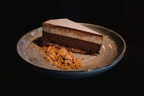 A slice of layered chocolate cake on a plate with crumbs beside it.