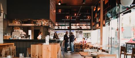 A modern cafe with wooden furniture, a bar area, and large windows offering a view of the street.