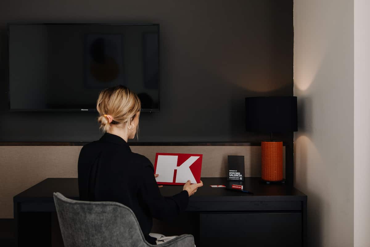 En person sidder ved et skrivebord med et fladskærms-tv, et rødt og hvidt skilt, en sort lampe og en lille æske.