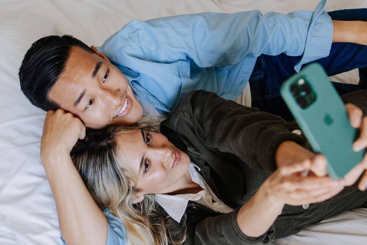Et par ligger på sengen med en smartphone.