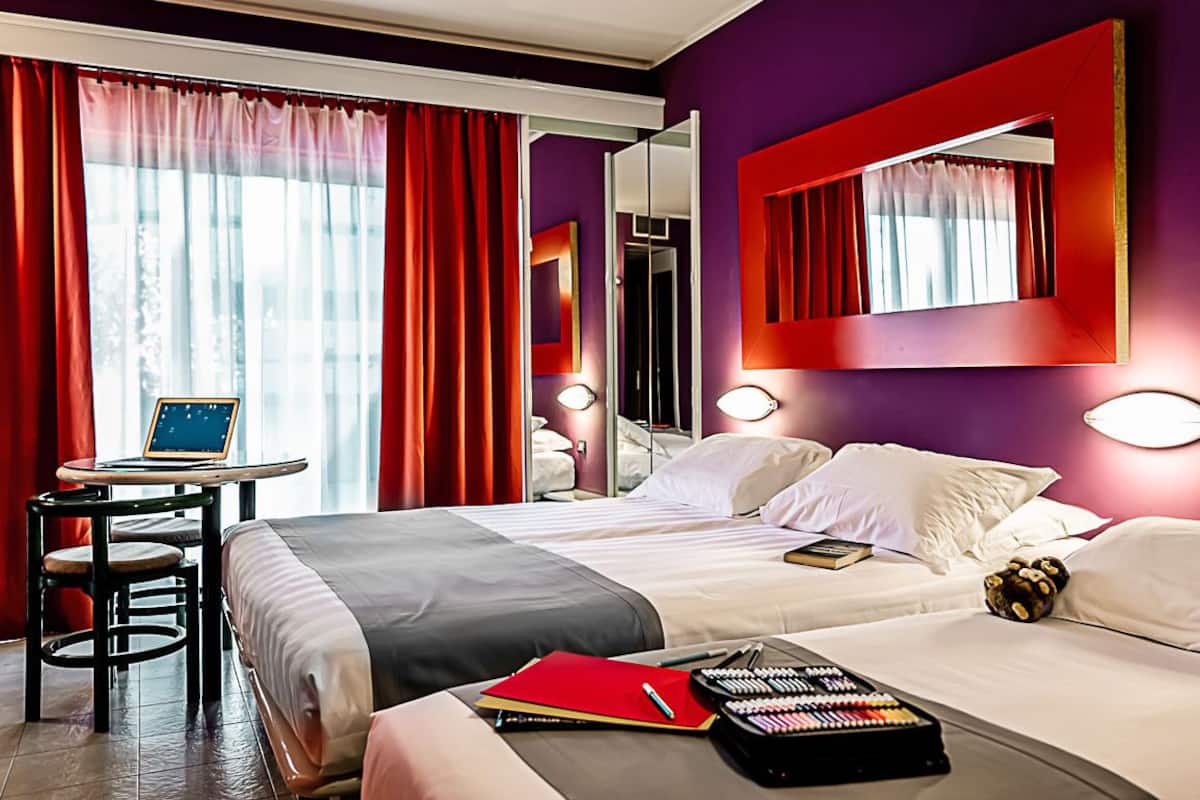 Une chambre d’hôtel comprenant un lit, un bureau avec un ordinateur portable, une chaise et une table de chevet avec une lampe.