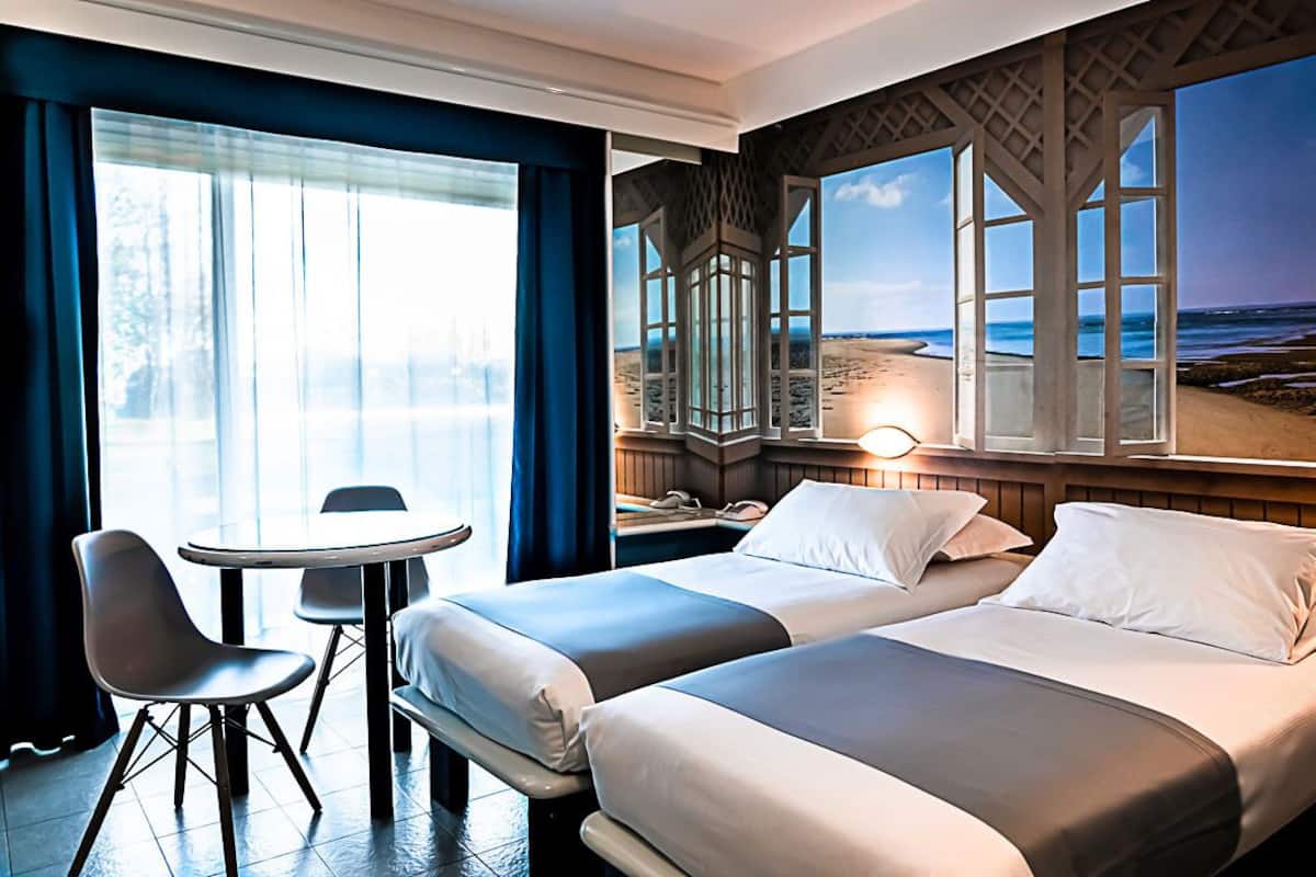 Une chambre d’hôtel avec deux lits, une table ronde et vue sur la plage.