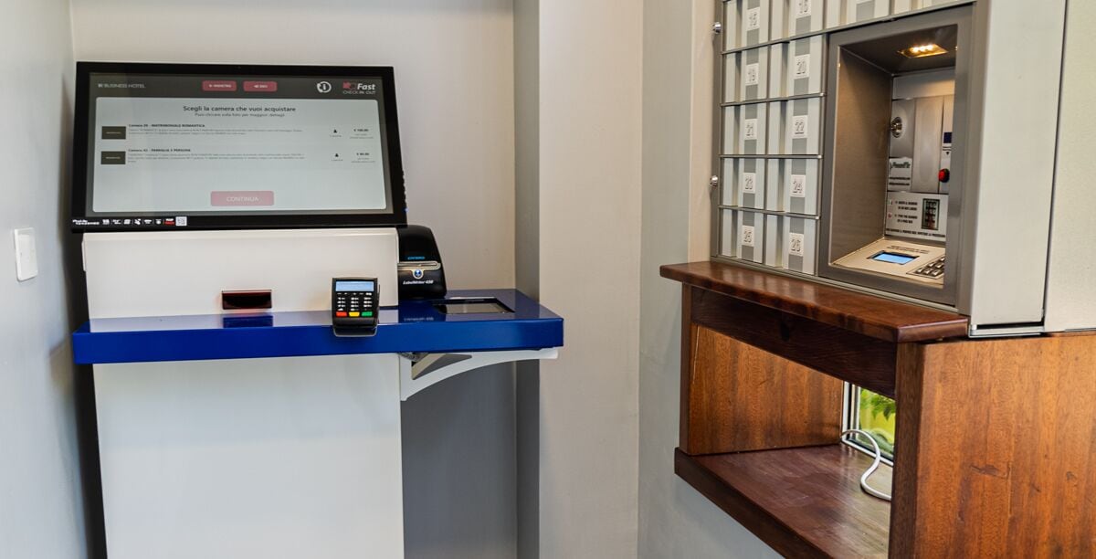 A hotel reception desk with a digital screen, a phone, and a self-service kiosk.