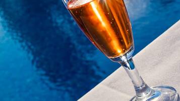 Ein Glas bernsteinfarbige Flüssigkeit neben einer Schale goldbraun frittierter Snacks am Pool.