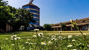 A building with a modern design, surrounded by a grassy area with daisies. - Business Hotel (Casale Monferrato)