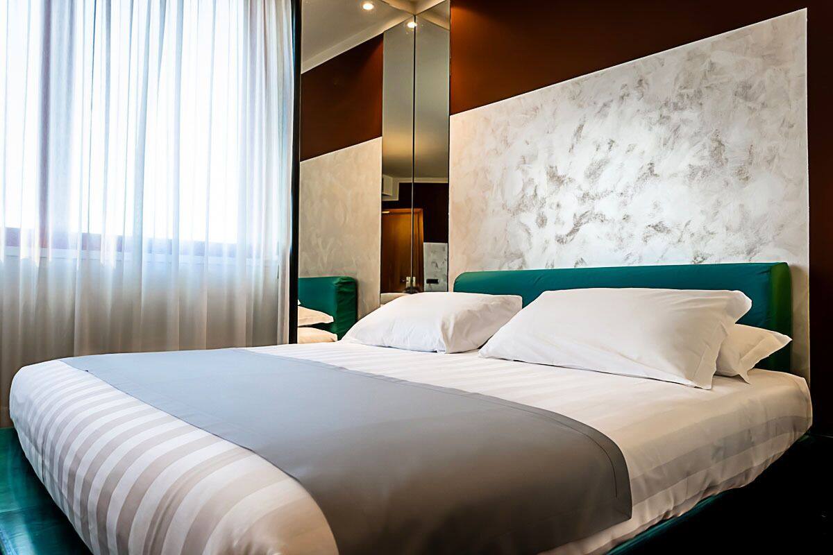Une chambre d’hôtel avec un grand lit, une tête de lit verte et un grand miroir au mur.