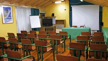 Une salle de classe avec des rangées de bureaux et de chaises, un écran de projection, un tableau blanc et un téléviseur.