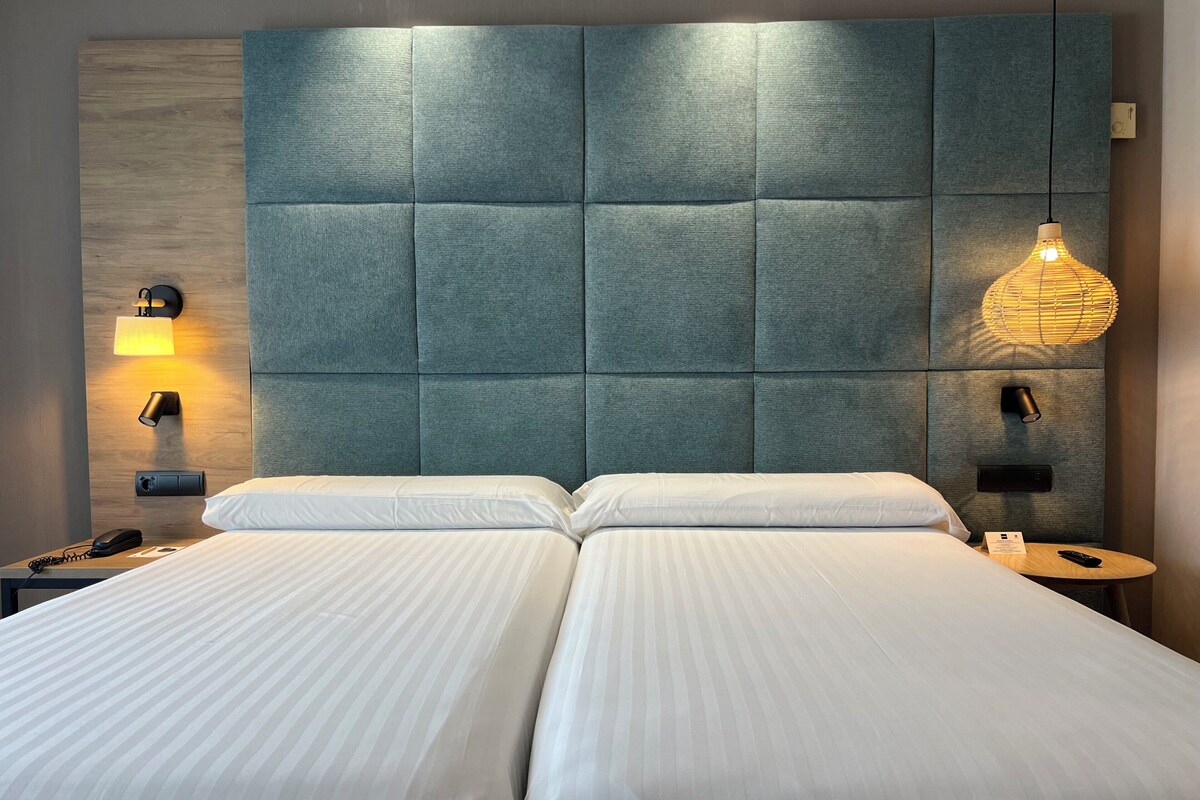 A double bed with a headboard, two bedside tables, a lamp, and a phone on the left side.