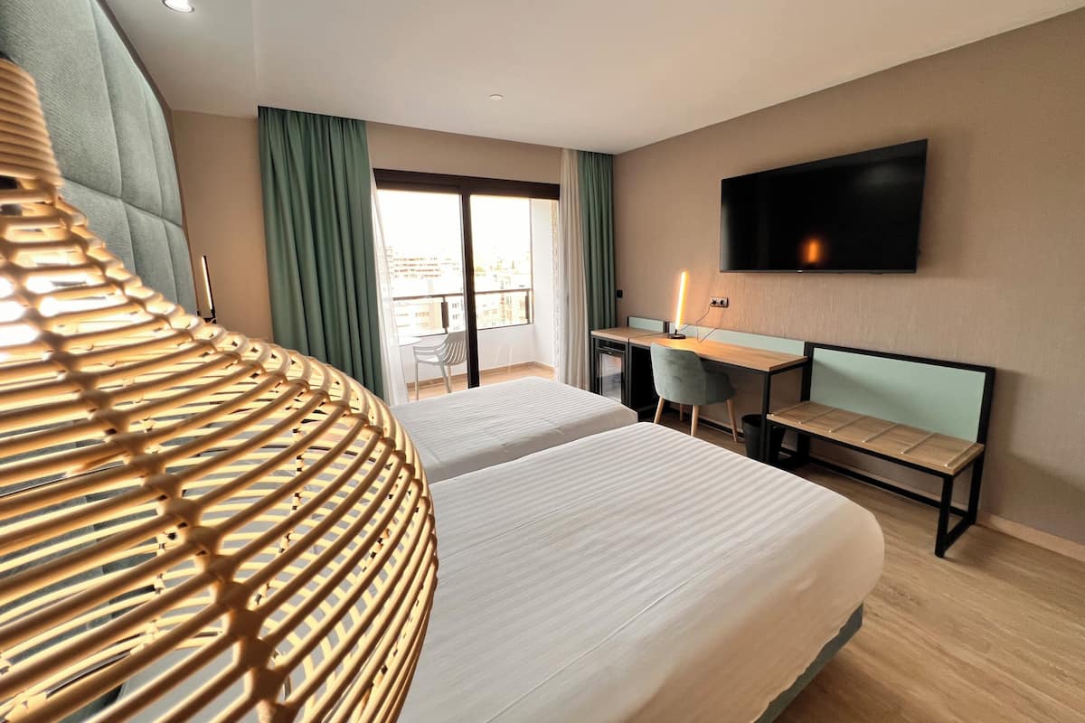 Habitación de hotel con dos camas, un escritorio, una silla, un televisor y un balcón con cortinas.