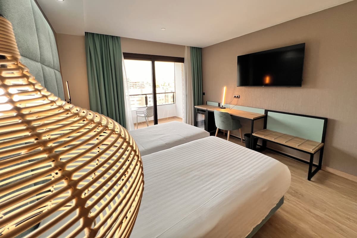 A hotel room with two beds, a desk, a chair, a TV, and a balcony with curtains.