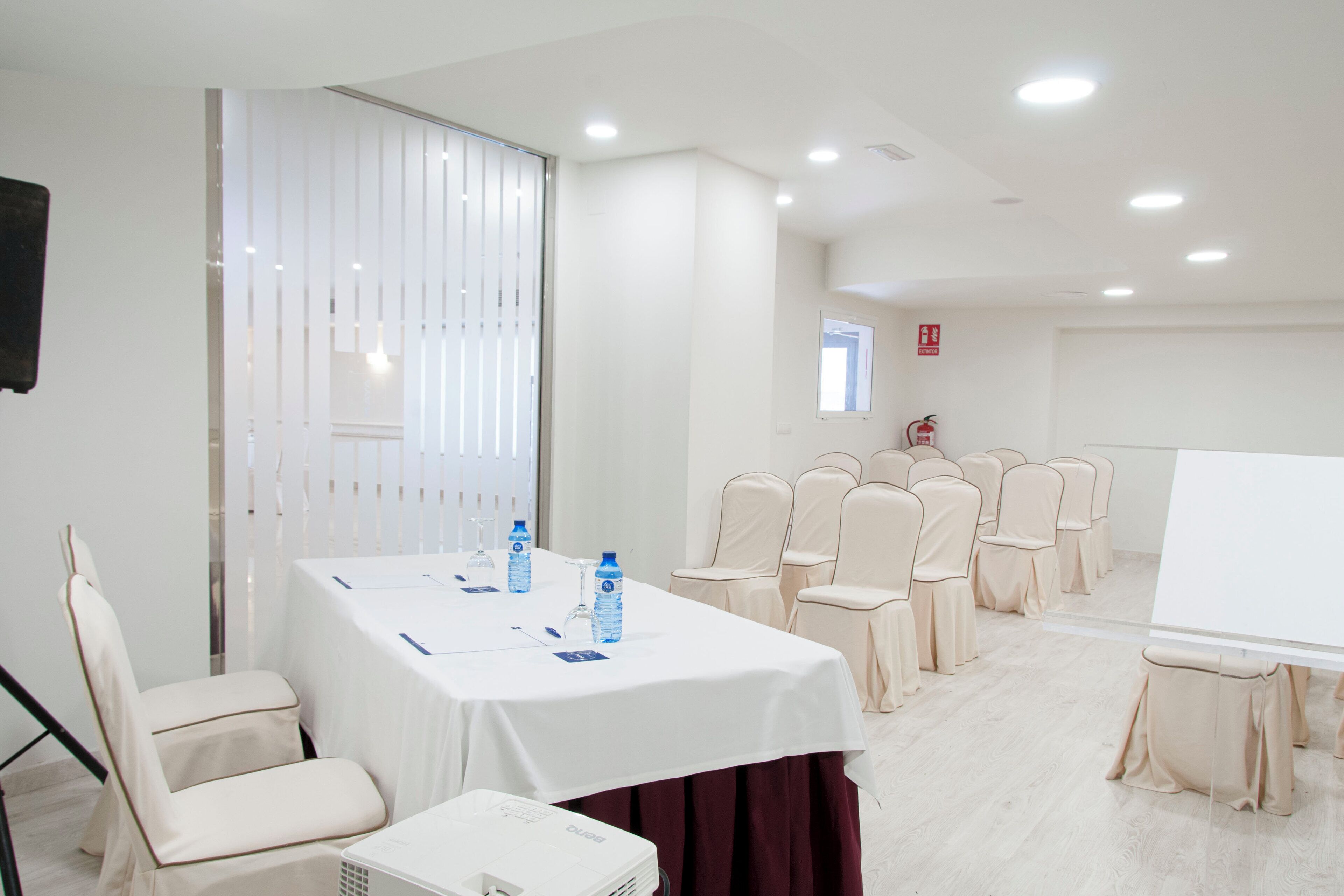 Une salle de conférence avec une table blanche, des chaises et un tableau blanc.
