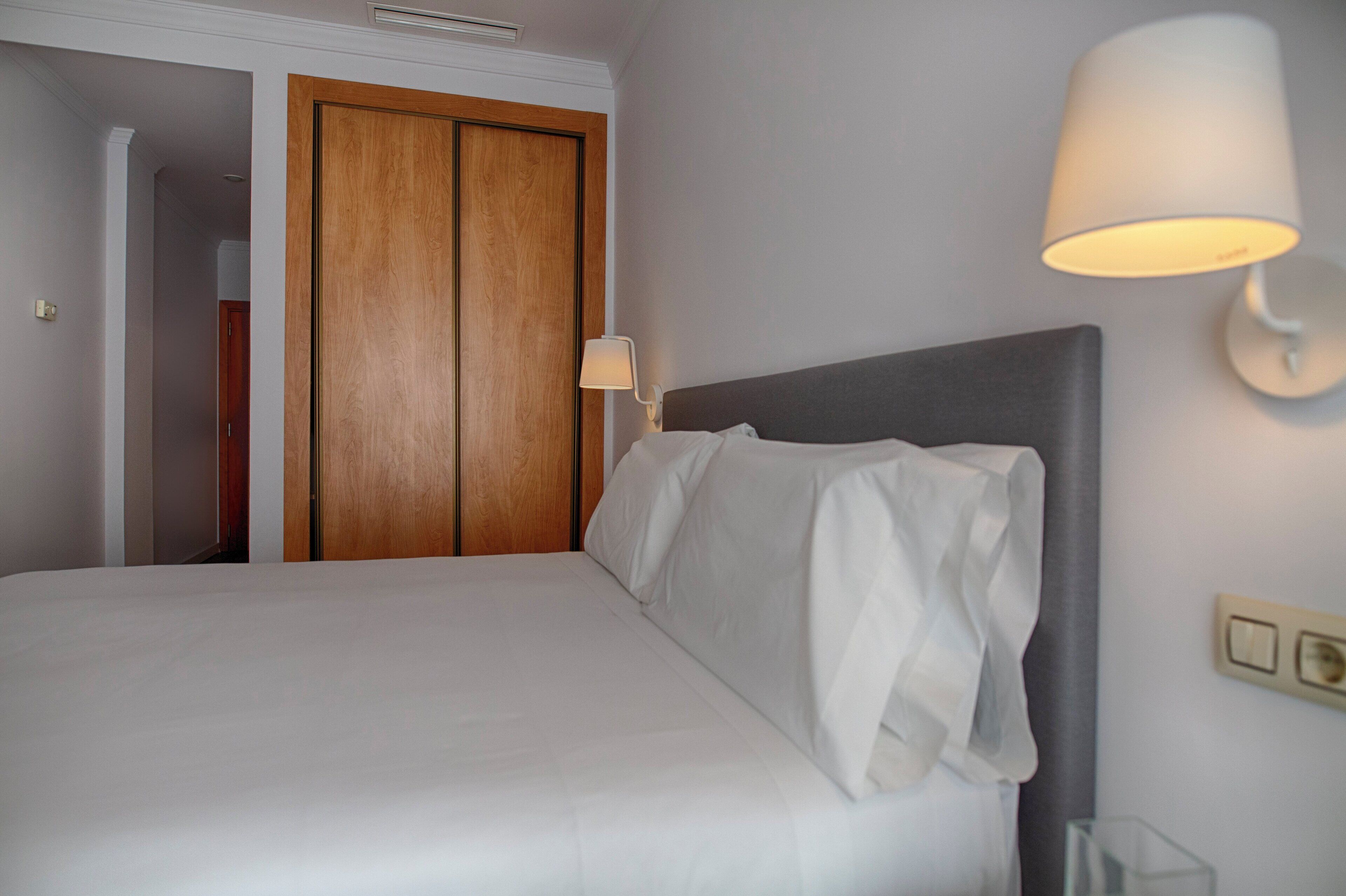 Une chambre d’hôtel avec un lit, une porte en bois, une lampe fixée au mur et un interrupteur.