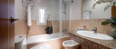 A bathroom with a toilet, bidet, bathtub, and a sink with a mirror.