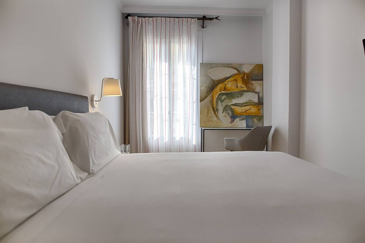 Habitación de hotel con una cama grande, un escritorio, una silla, una lámpara y un cuadro en la pared.