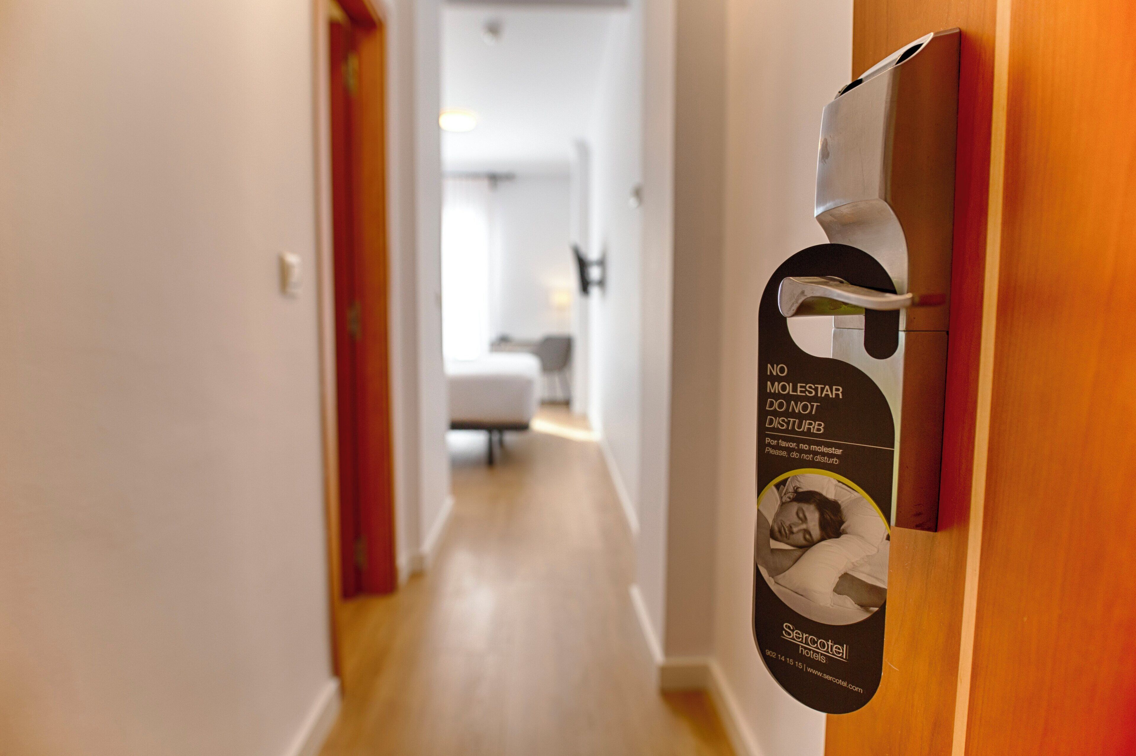A hallway with a door featuring a sign that reads 'NO MOLESTAR DO NOT DISTURB' and 'Sercotel hotels.'