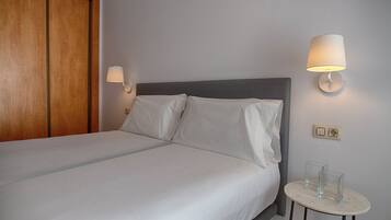 A neatly made bed with white linens, a wooden wardrobe, and two wall-mounted lamps.