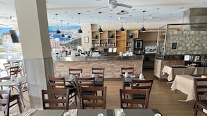 Restaurante com mesas preparadas para refeições, área de bar e vista panorâmica da cidade.