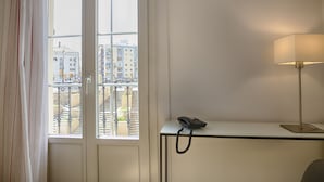 Quarto de hotel com escrivaninha, telefone e janela com vista para edifícios e uma escadaria.