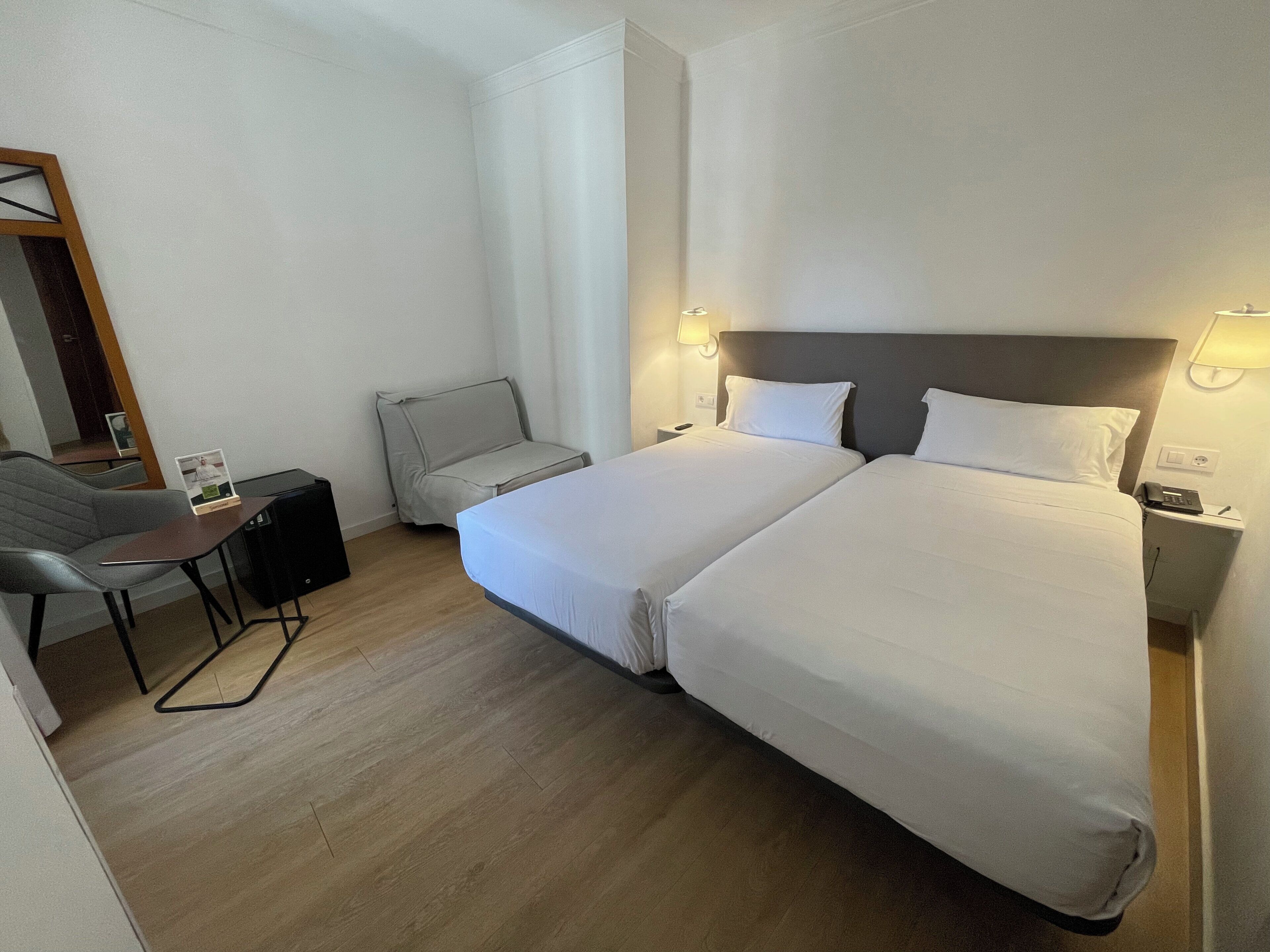 Habitación de hotel con dos camas, un escritorio, una silla, una lámpara y un teléfono en la mesita de noche.