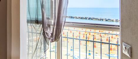 Una habitación con un ventanal grande con vistas a la playa, una mesita con un plato y una botella, y un televisor montado en la pared.