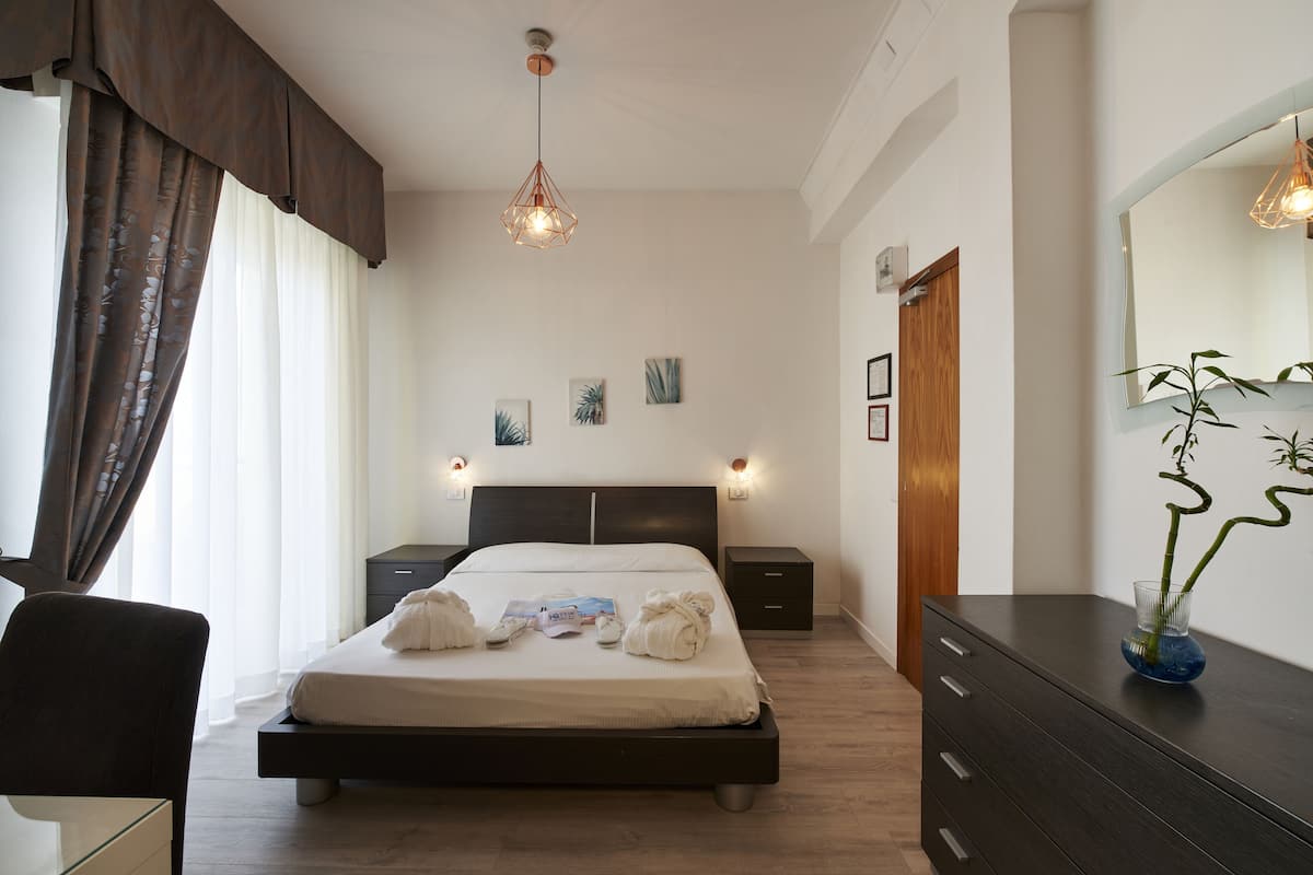 A modern hotel room with a large bed, bedside tables, a desk, and a dresser.