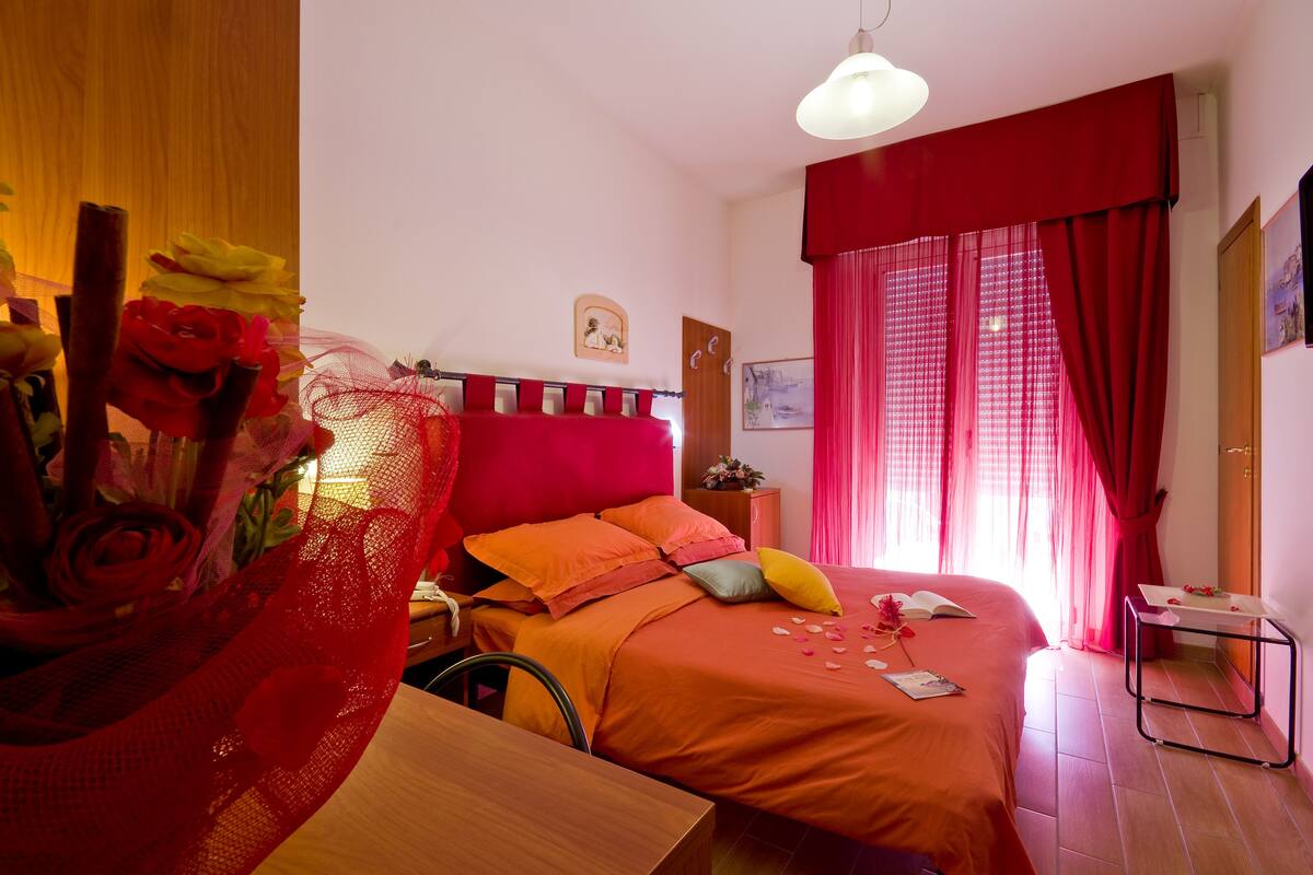 A bedroom with a bed, a bedside table, a chair, a desk, and a window with curtains.
