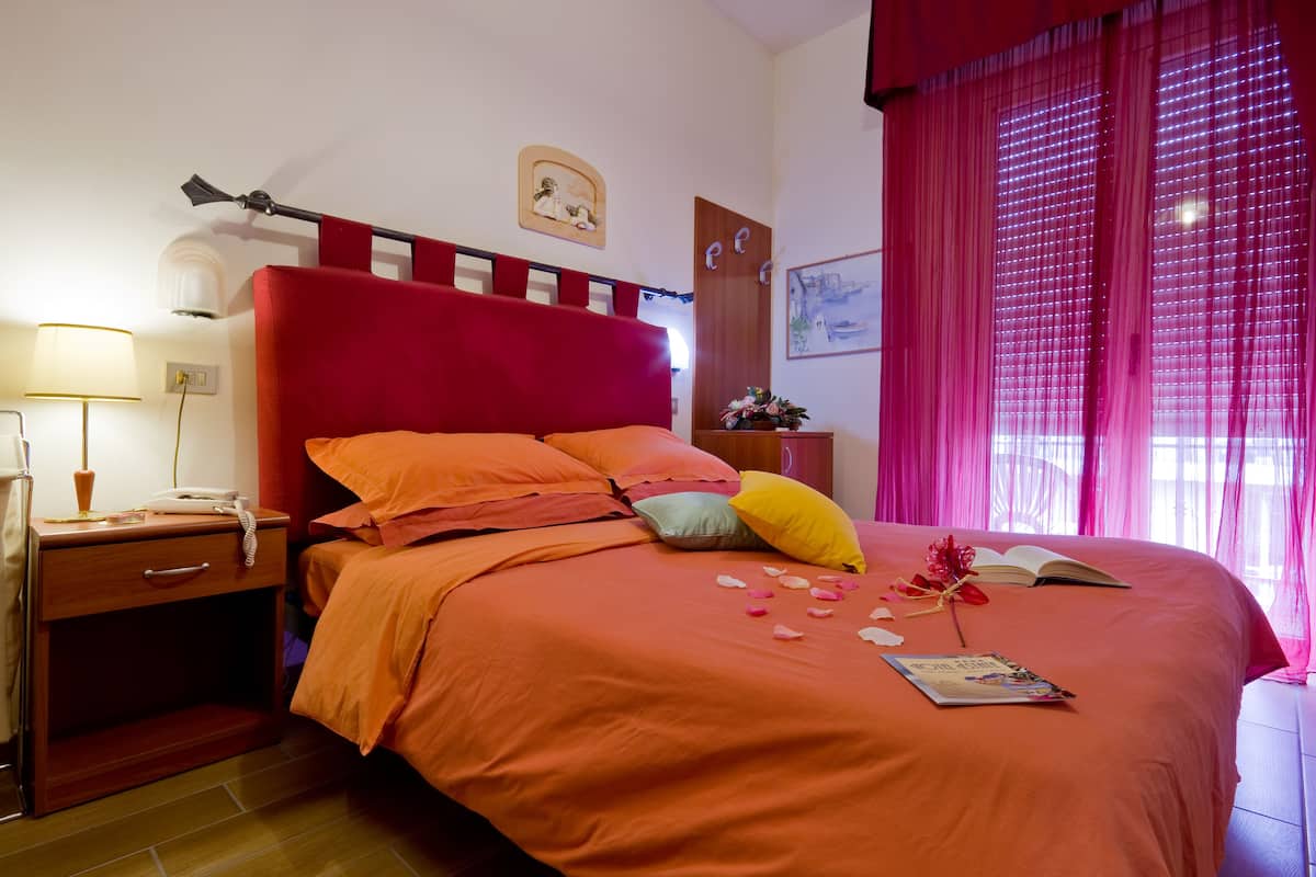 A neatly made bed with a red headboard, a bedside table with a lamp, and a window with pink curtains.