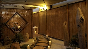 A stone pathway lined with candles leading to a wooden structure with a lantern.